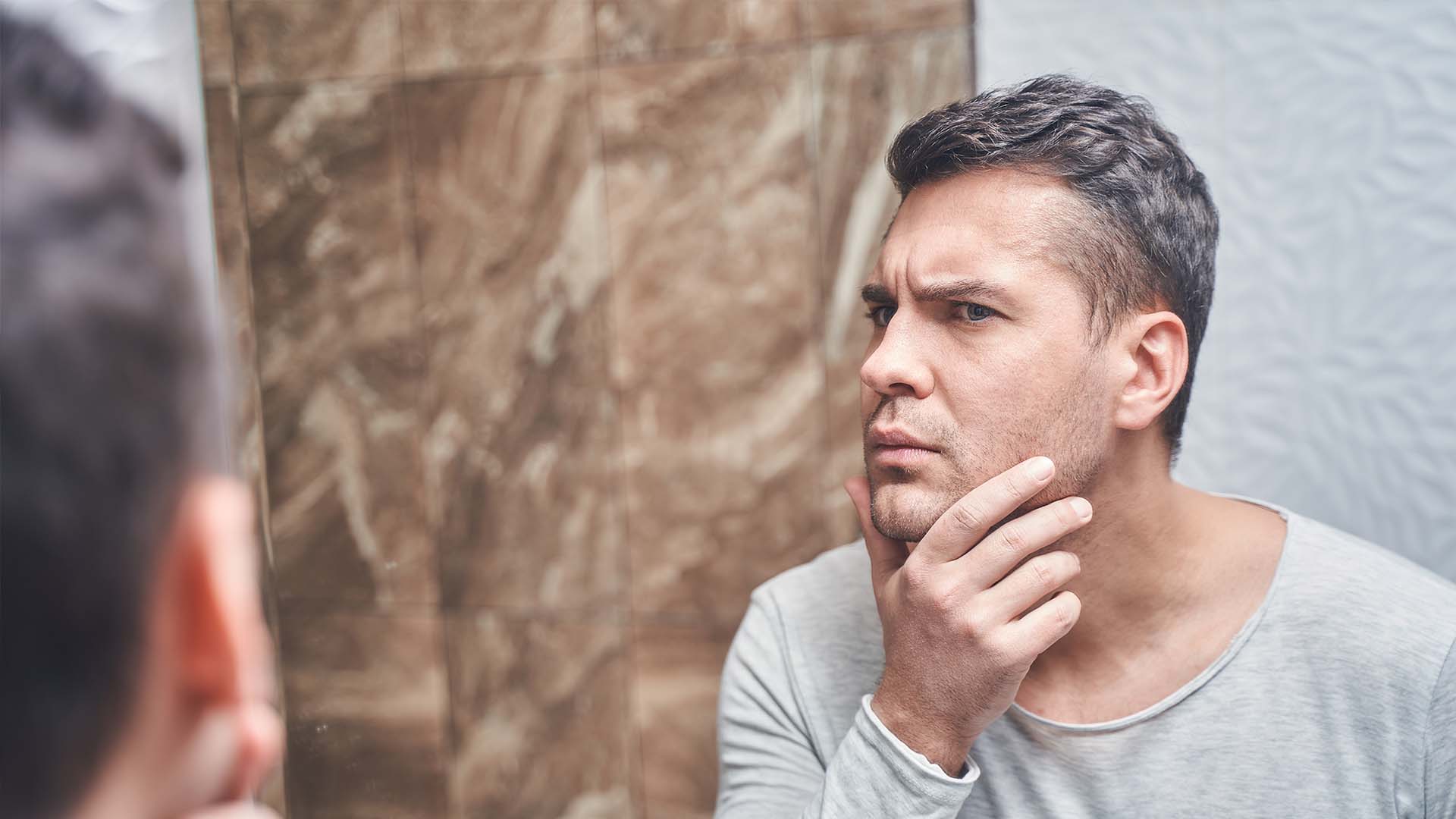 Man looking at himself in the mirror with a thoughtful expression, symbolizing self-reflection and navigating relationships with a narcissist