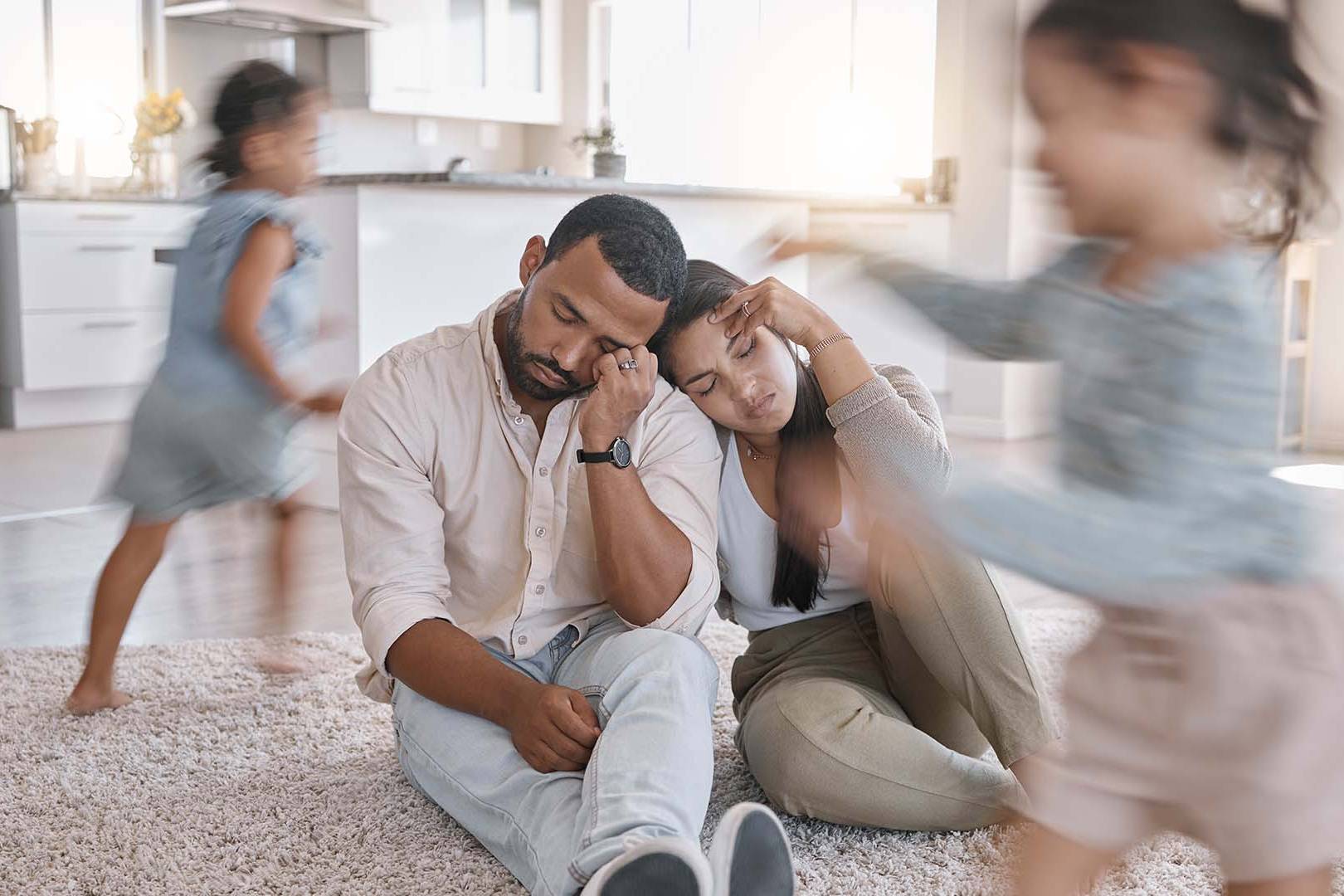Overwhelmed parents sitting on the floor while children run around them in a busy household, symbolizing the challenges of parenting with depression