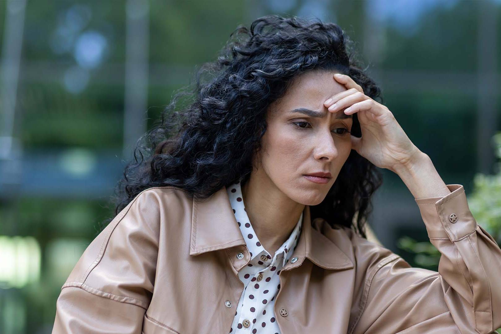 Thoughtful woman sitting outdoors with her hand on her head, symbolizing introspection and the challenge of differentiating sadness from depression