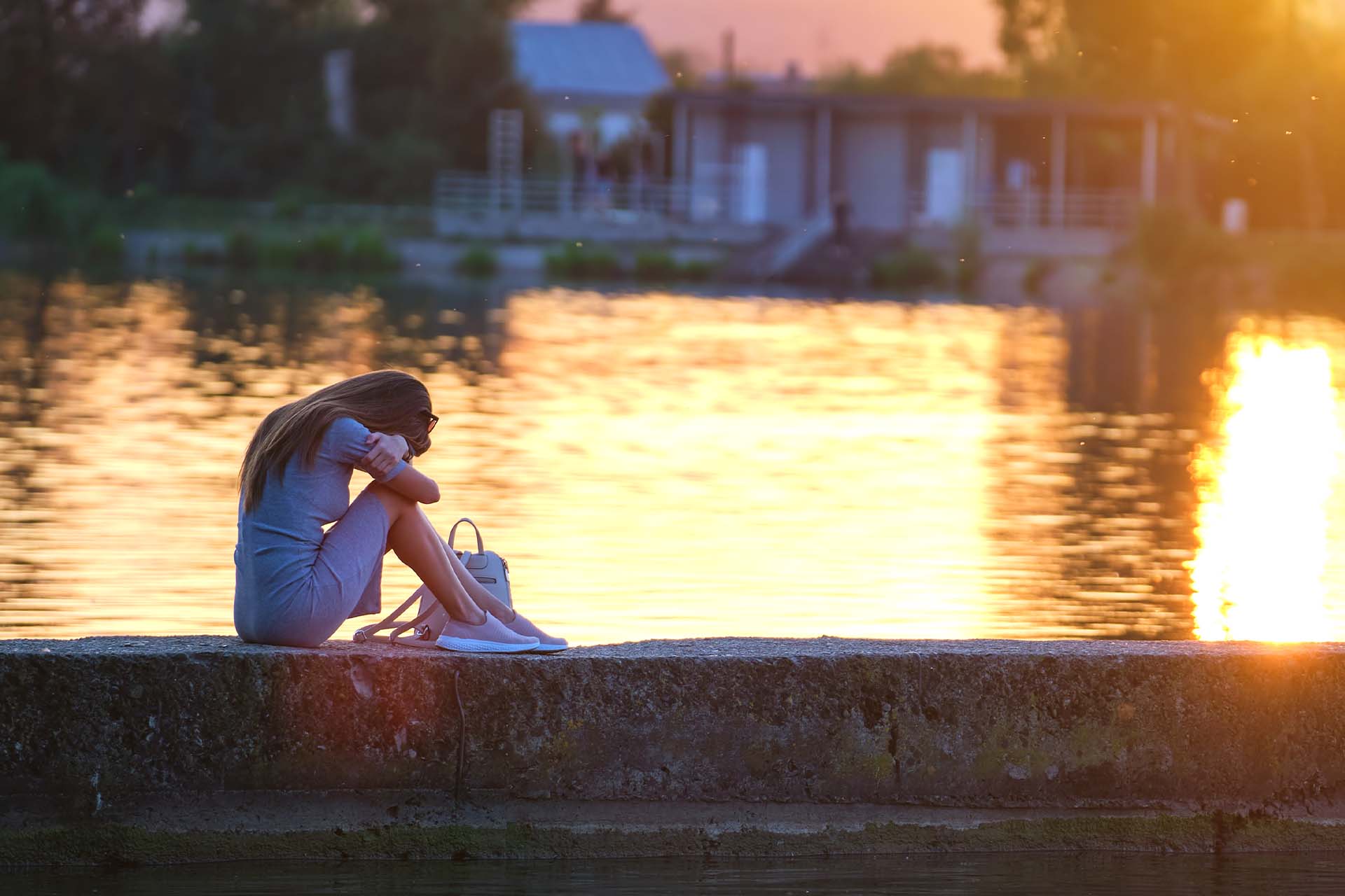 Woman sitting alone by the water at sunset, symbolizing the introspection and isolation often felt with Reverse Seasonal Affective Disorder.