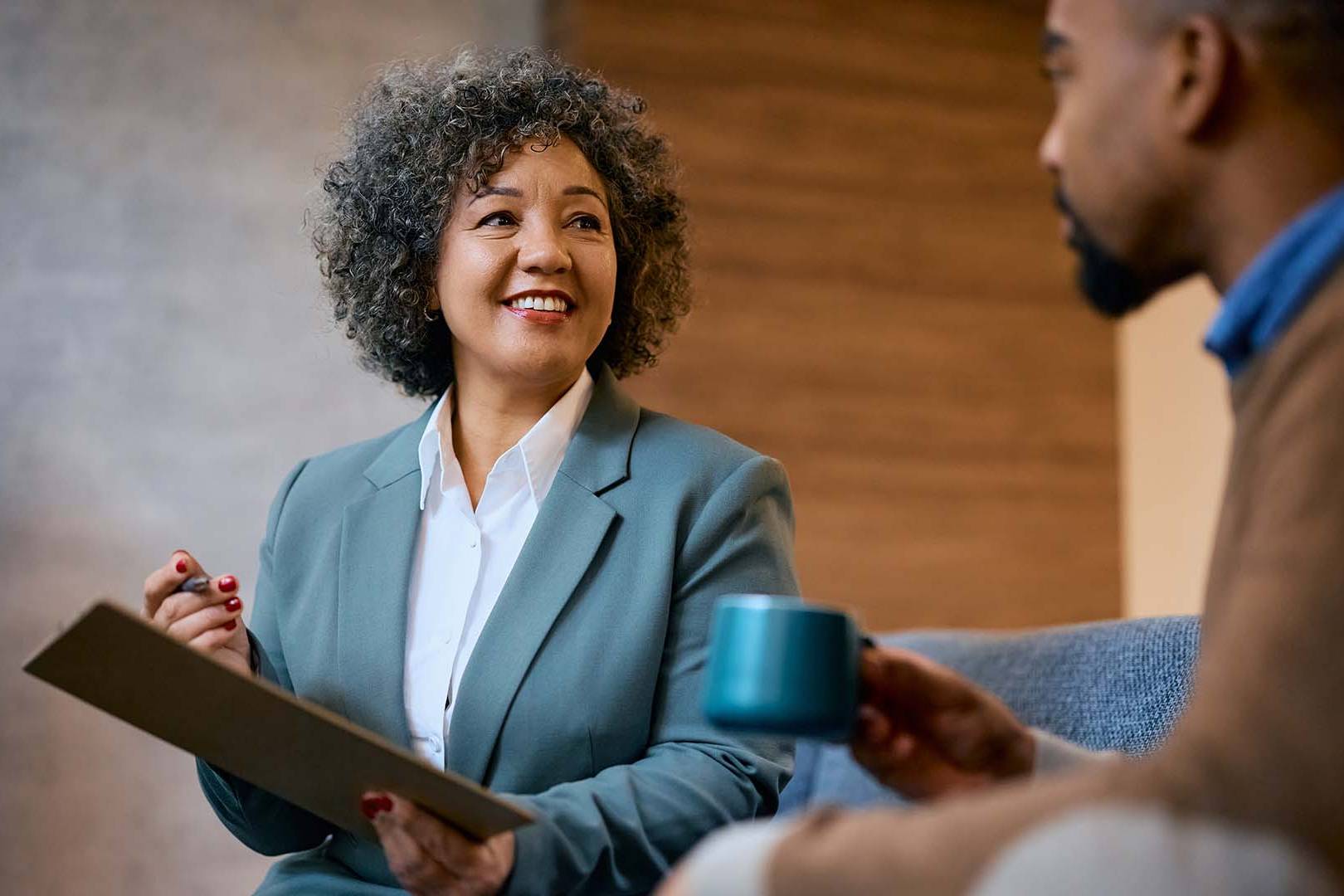 A smiling therapist engaging in a motivational interviewing session with a client, holding a clipboard in a warm, professional setting.