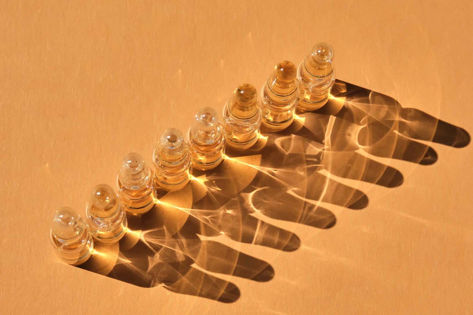 Seven clear glass vials casting intricate shadows on a beige background, symbolizing structure, precision, and the nuanced differences between OCD and OCPD