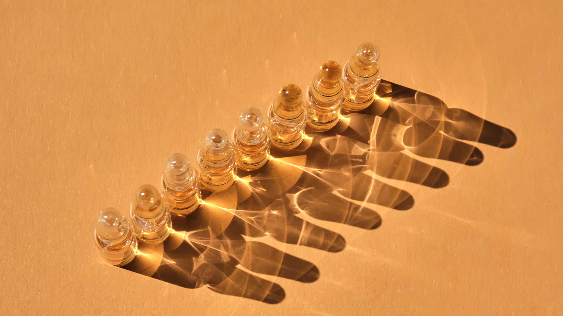 Seven clear glass vials casting intricate shadows on a beige background, symbolizing structure, precision, and the nuanced differences between OCD and OCPD