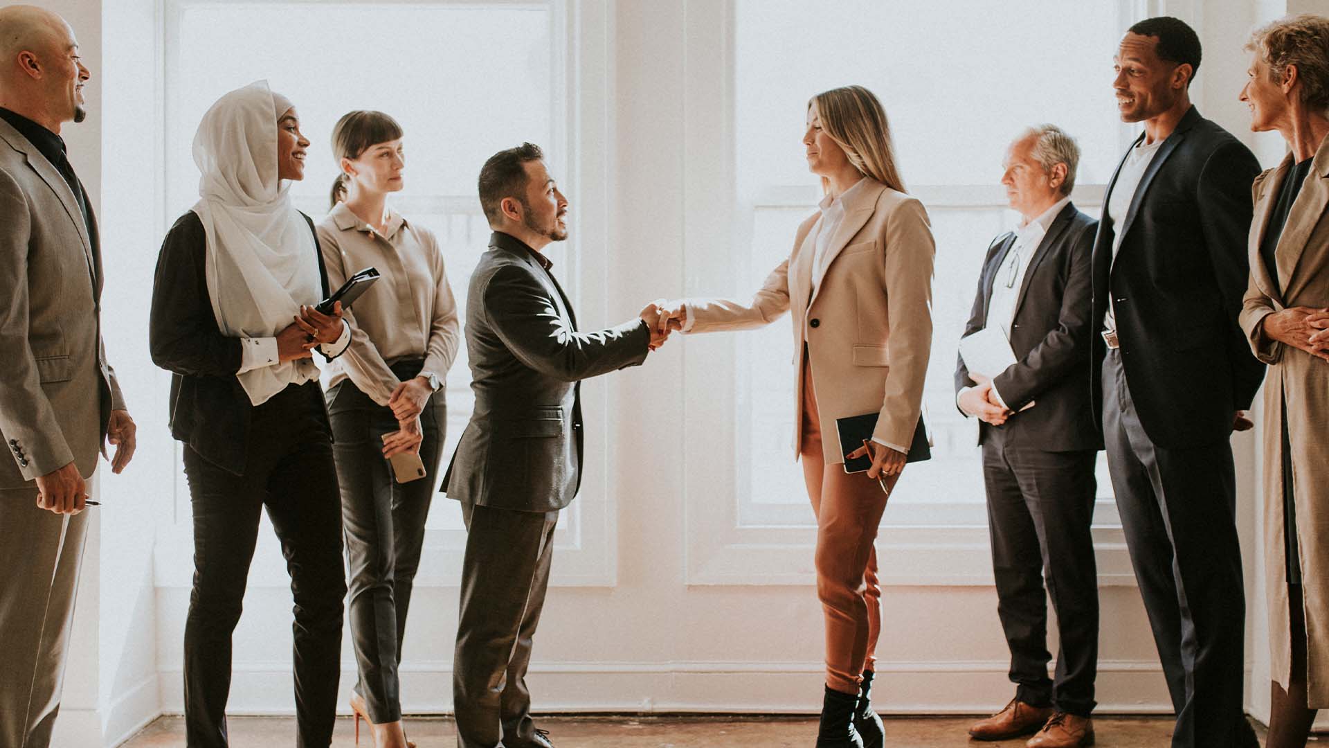 A diverse group of professionals smiling and shaking hands in a bright room, symbolizing collaboration, acceptance, and successful integration within therapeutic practices.