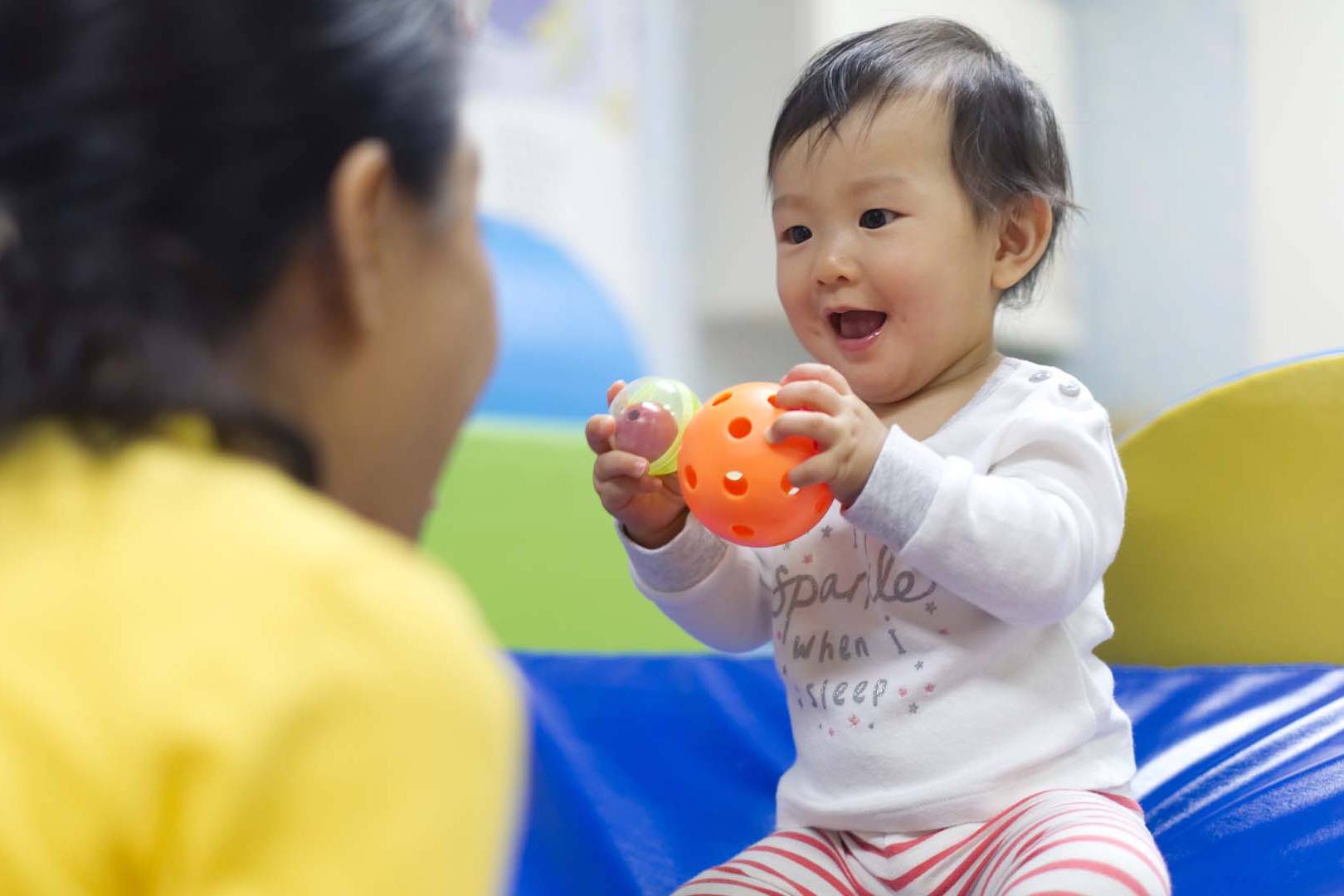 A happy baby playing with sensory balls during a developmental therapy session, guided by a therapist focusing on early cognitive and motor skills.