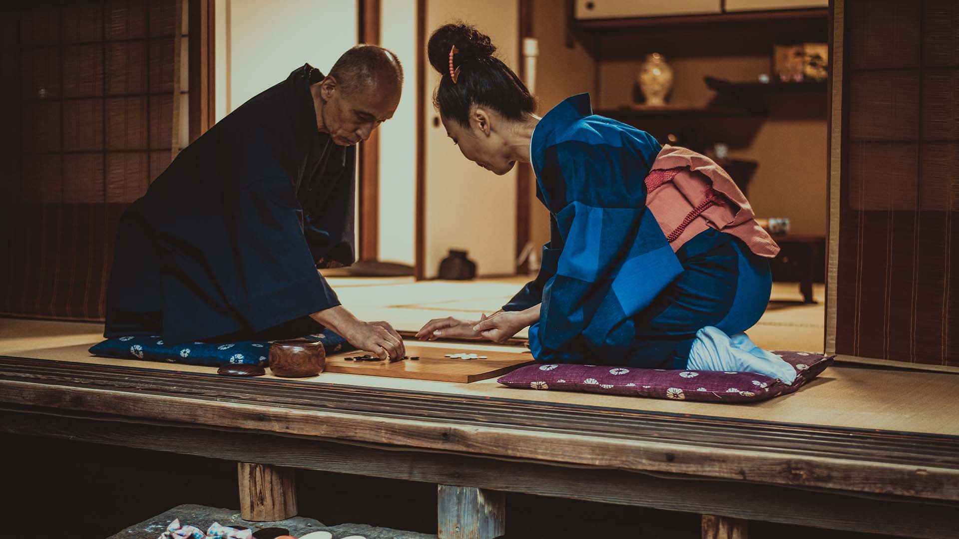 Two individuals wearing traditional Japanese attire engage in a mindful game of Go inside a traditional room, symbolizing the reflective practices central to the Hakomi Method.