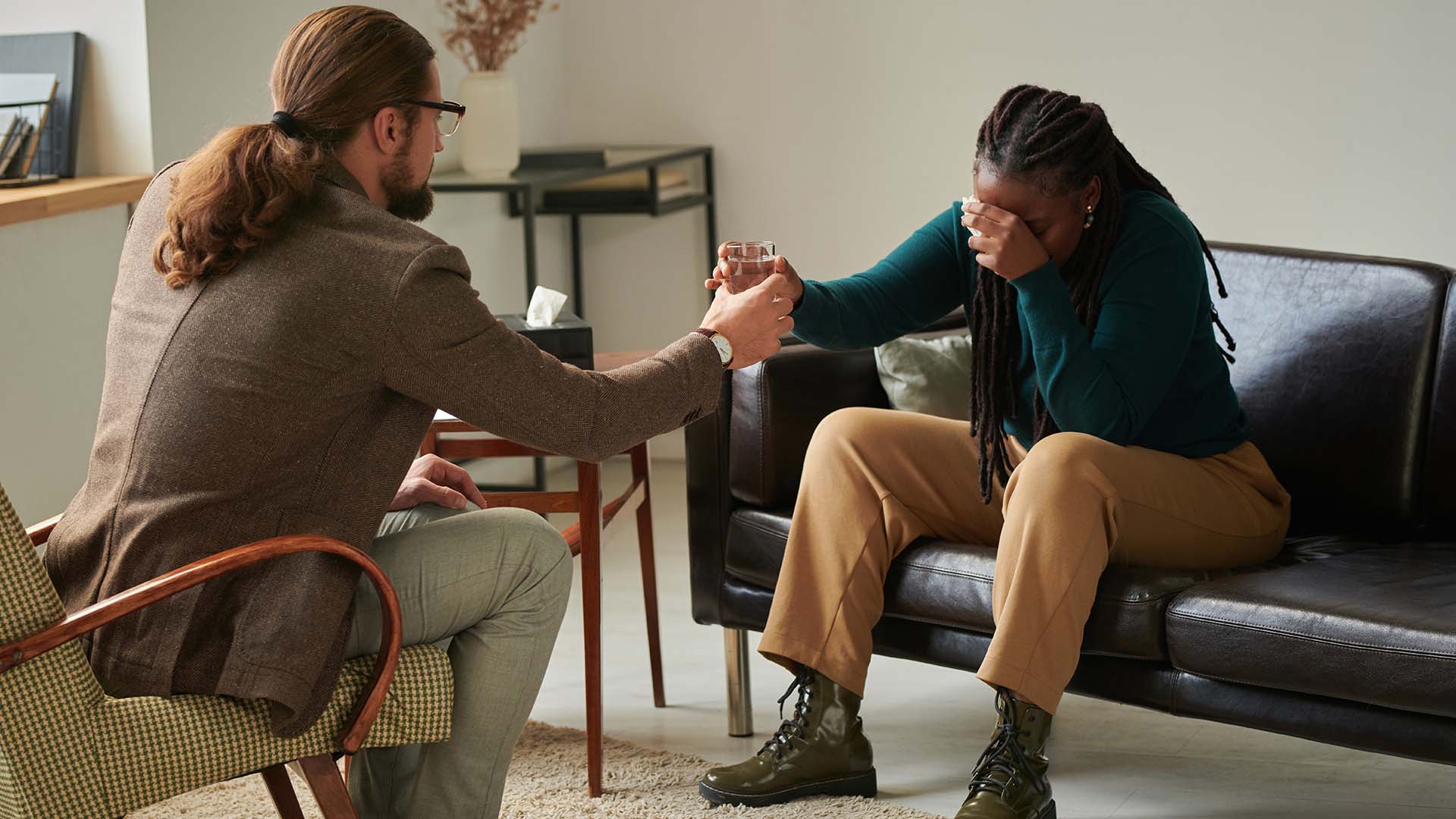 A therapist offering a glass of water to a distressed client during an embodied psychotherapy session, symbolizing care and holistic emotional healing through the mind-body connection.