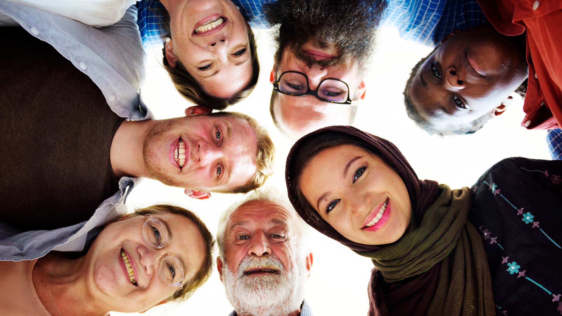 A diverse group of individuals standing in a circle, smiling warmly and looking down at the camera, symbolizing connection, shared experiences, and emotional healing.