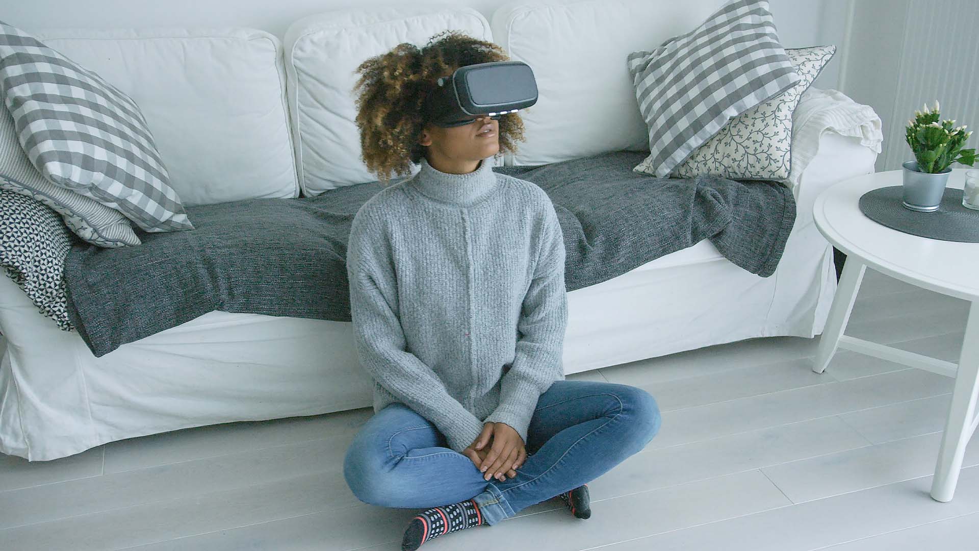 A woman sitting cross-legged on the floor in a cozy living room, wearing a VR headset, engaging in immersive therapy or virtual mental health support.
