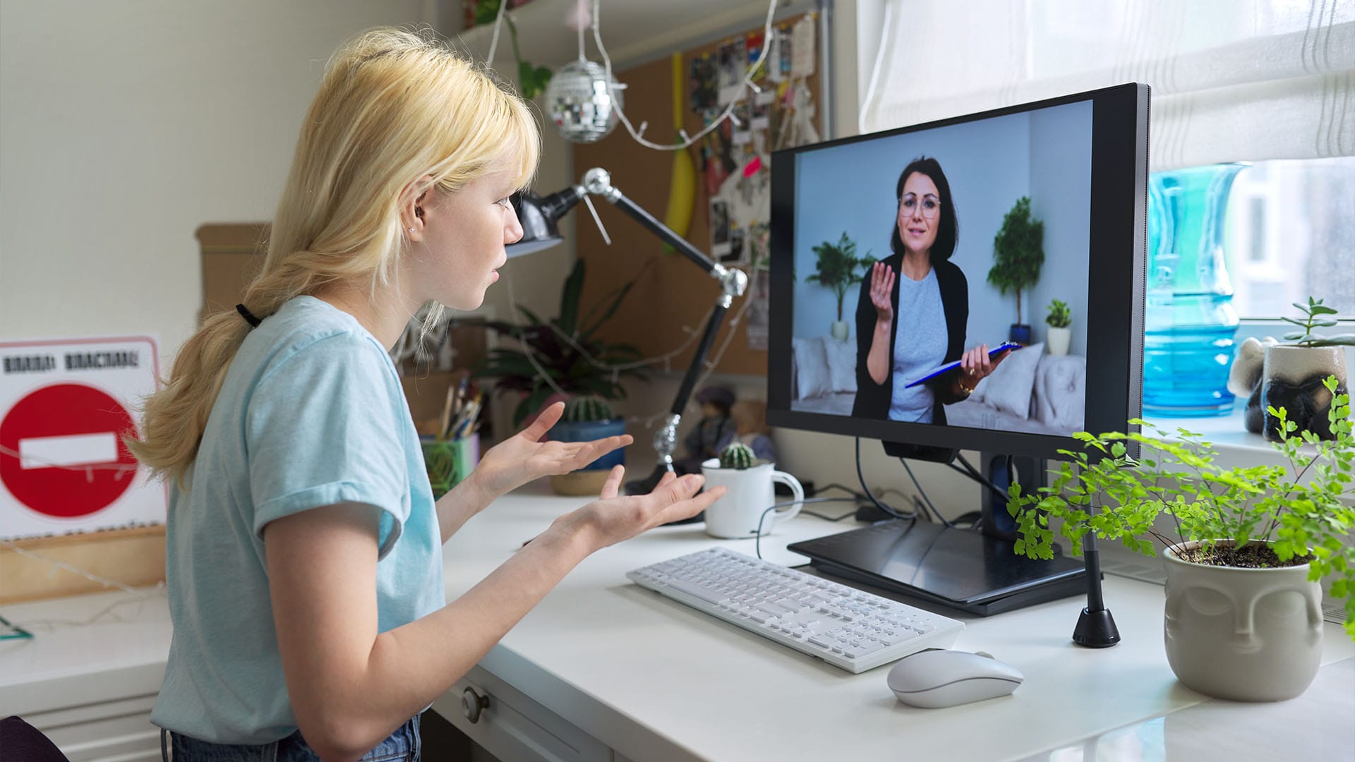 Young woman in a virtual therapy session expressing emotion, speaking with her therapist through a monitor.