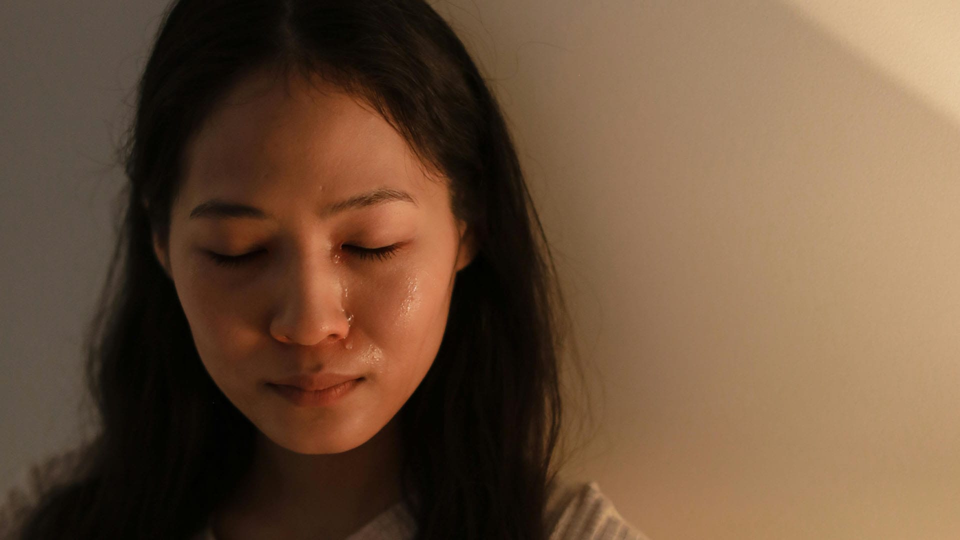Close-up of a young woman with closed eyes and tears on her cheeks, expressing quiet sadness or emotional distress.