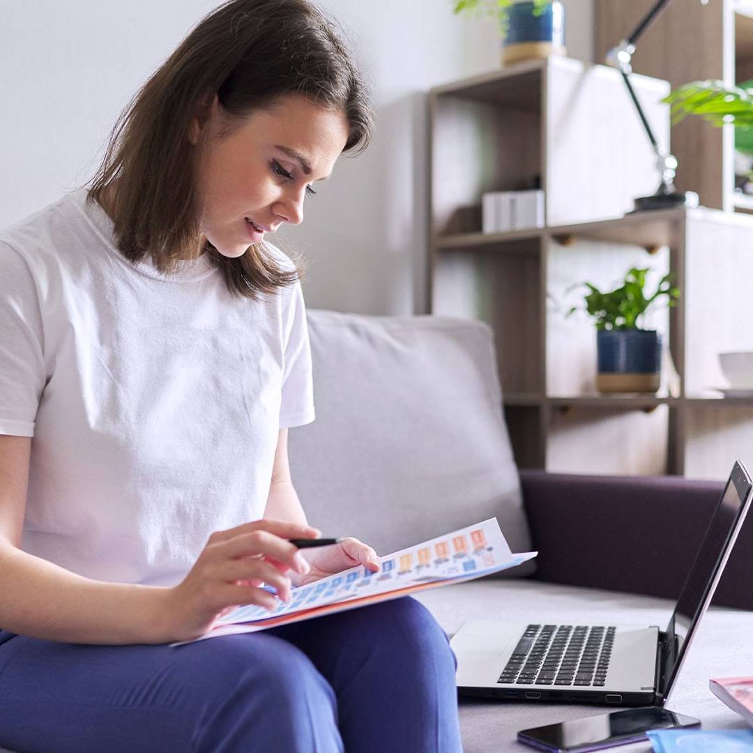 Woman sitting on a couch with open laptop, reviewing documents while appearing calm and focused.