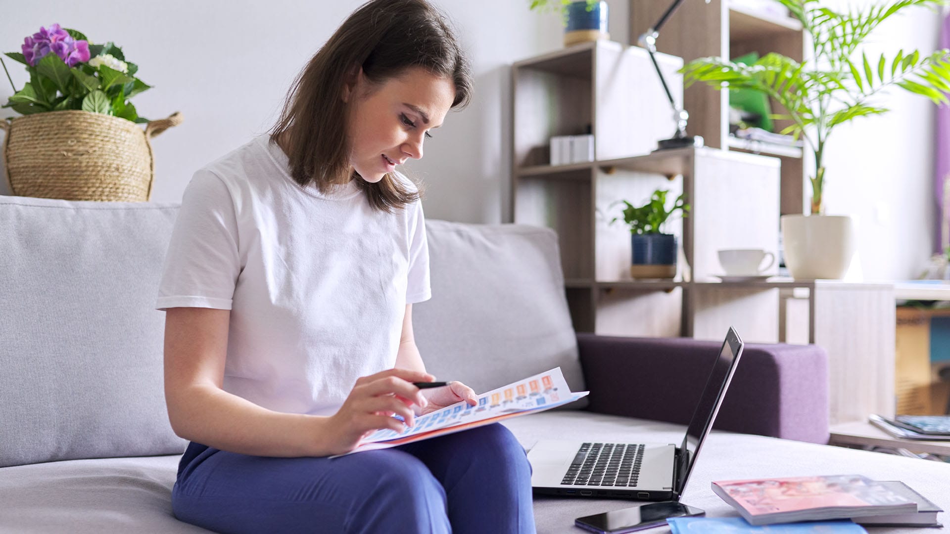 Woman sitting on a couch with open laptop, reviewing documents while appearing calm and focused.