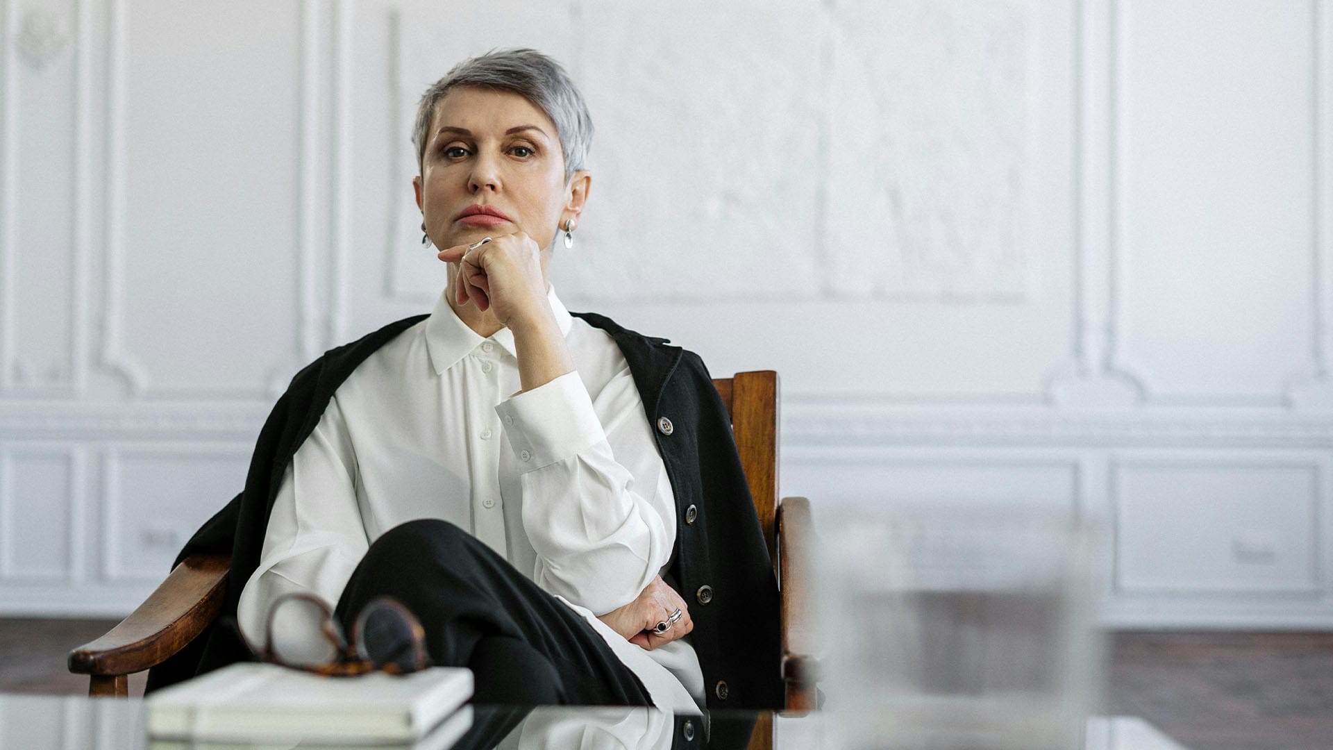 A poised therapist in a white blouse sits in a calm, elegant office, reflecting the confidence and safety offered through EMDR therapy for trauma recovery.
