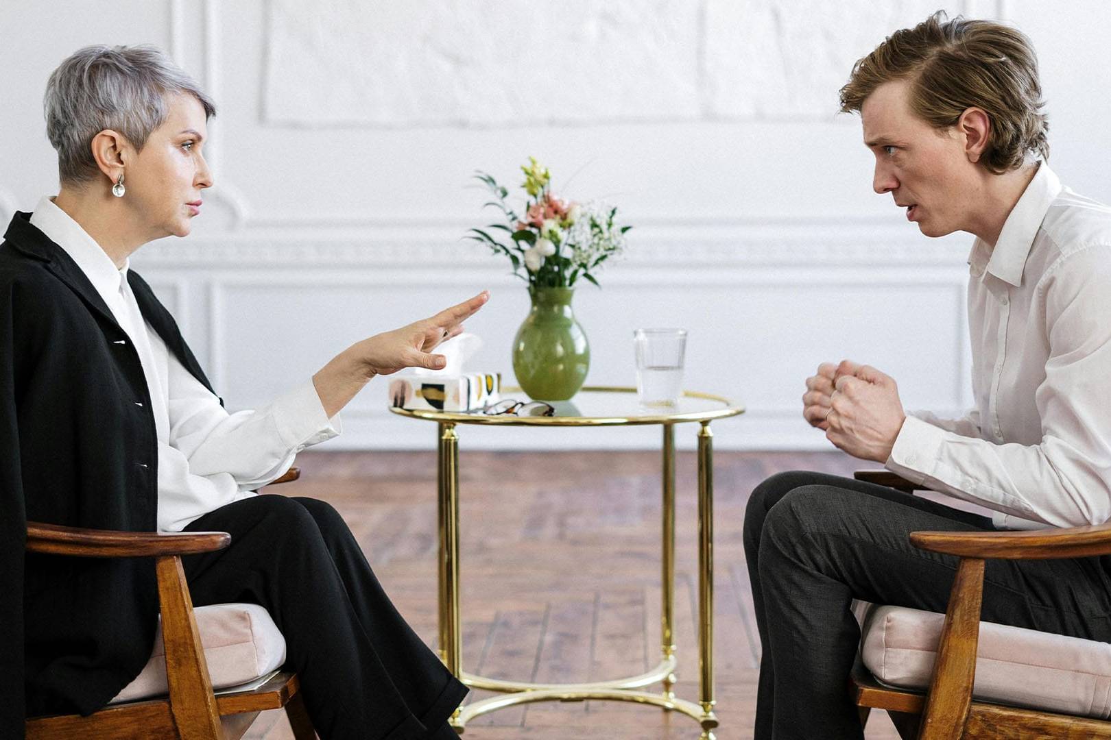 A therapist and a well-dressed man engage in a serious and private therapy conversation in a calm, upscale office setting.