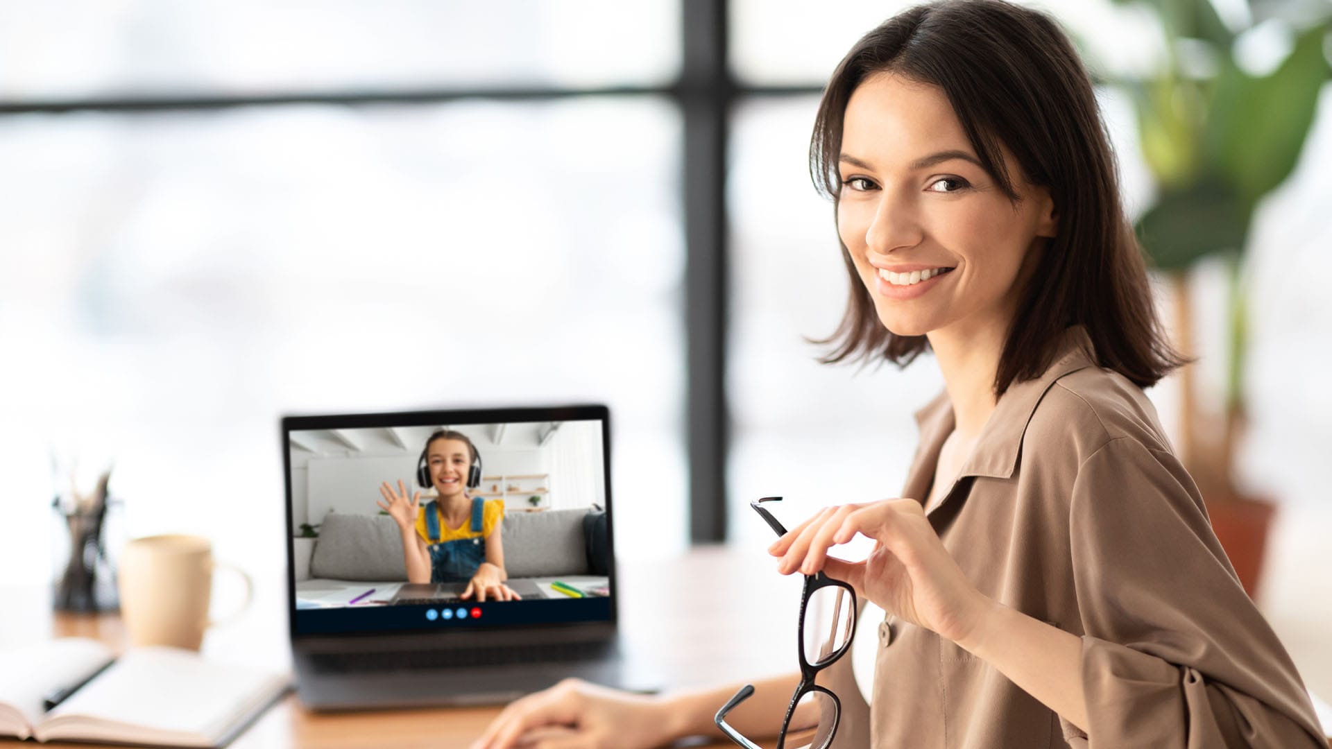 Smiling woman holding glasses during a video call with another cheerful woman on her laptop screen.