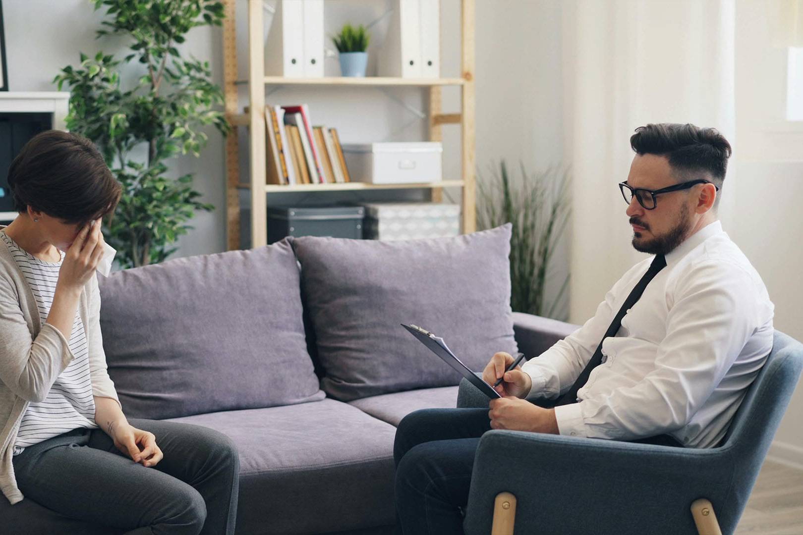Therapist attentively supporting a tearful client during a private therapy session in a modern, professional office setting.