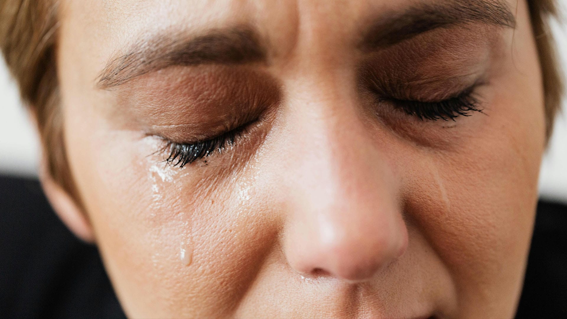A close-up of a woman with her eyes closed as tears stream down her face, capturing a moment of emotional release, grief, or vulnerability.