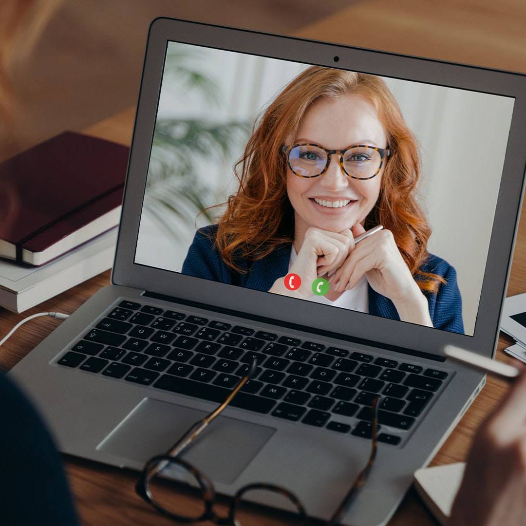 Person attending a virtual therapy session with a smiling therapist visible on a laptop screen.