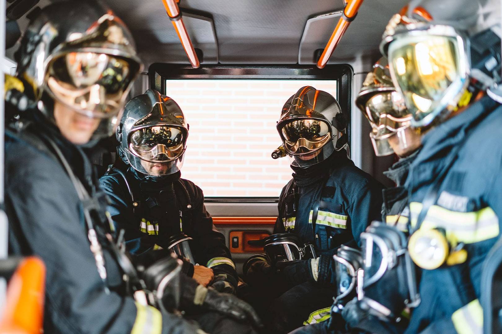 A team of Oxnard firefighters wearing reflective helmets and full protective gear sit inside a fire truck, looking outward with focused and ready expressions.