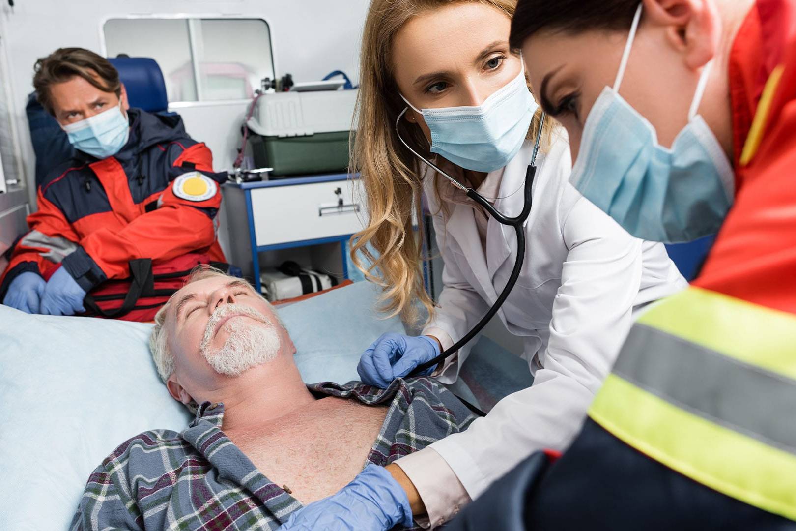 Paramedics and a doctor treat an unconscious elderly man in the back of an ambulance.