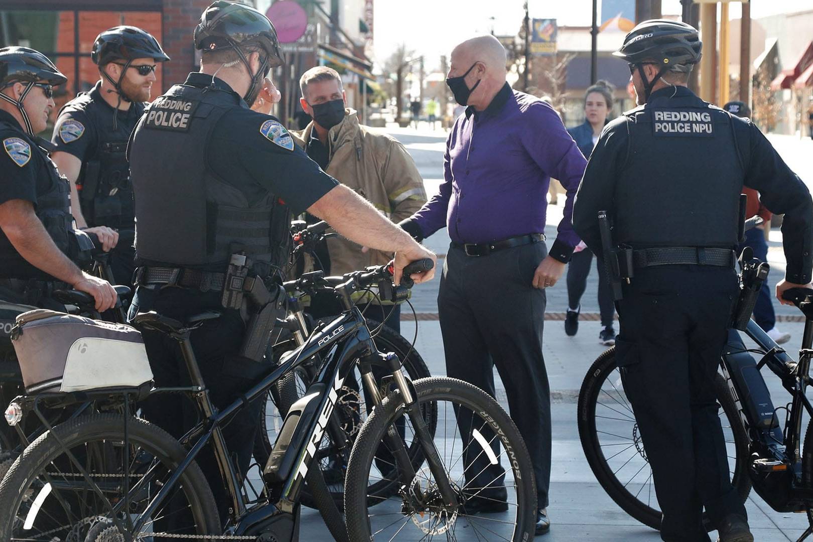Redding Police bike officers in tactical gear talking with civilians in a downtown area.