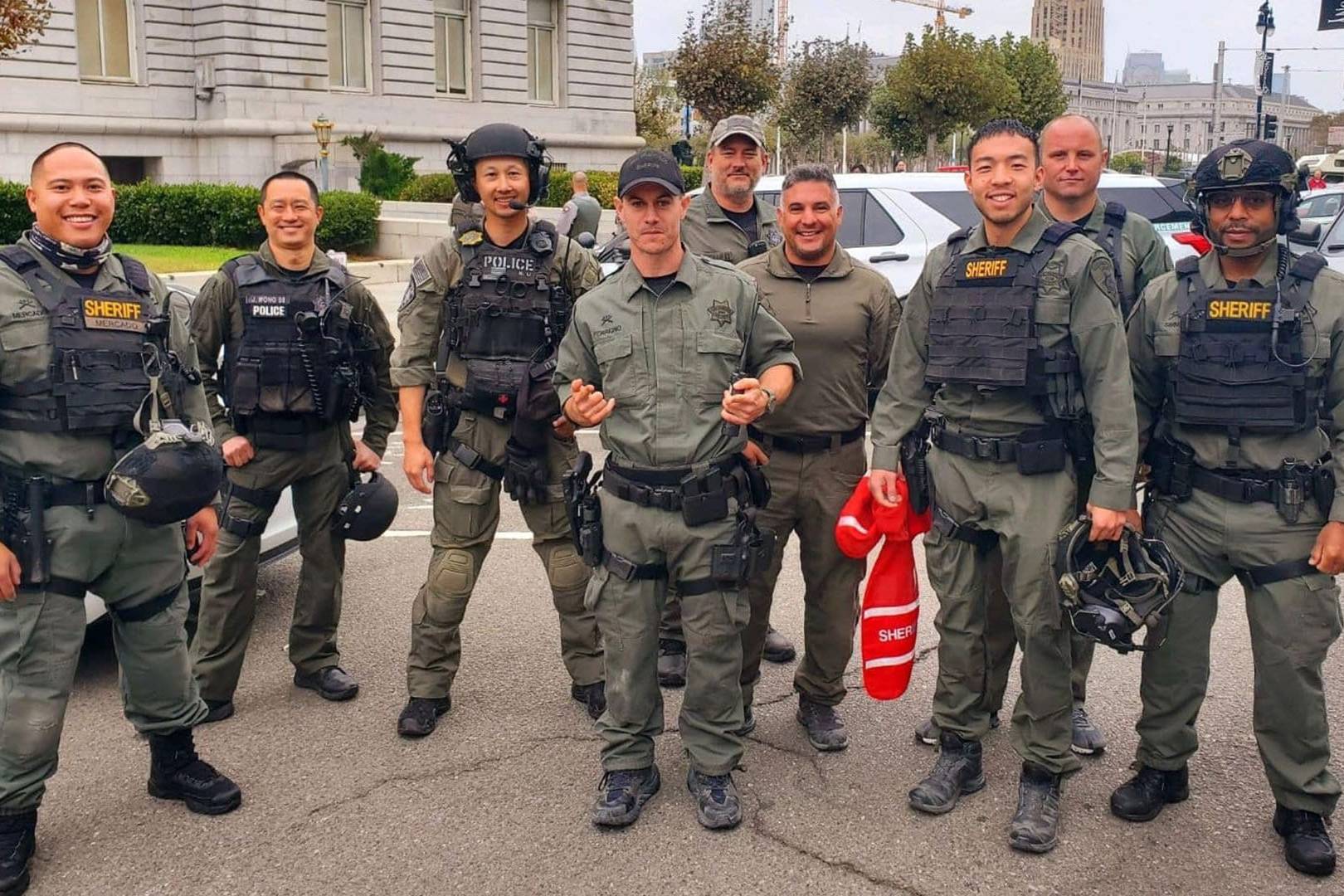 San Francisco Sheriff's deputies and tactical police officers posing together in uniform on a city street in front of government buildings.