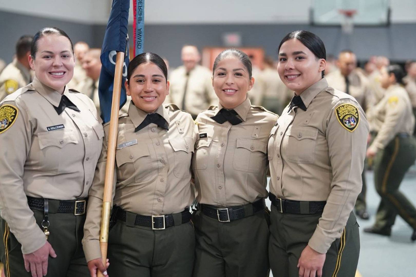 Four smiling California correctional officers pose together in uniform during a formal event.