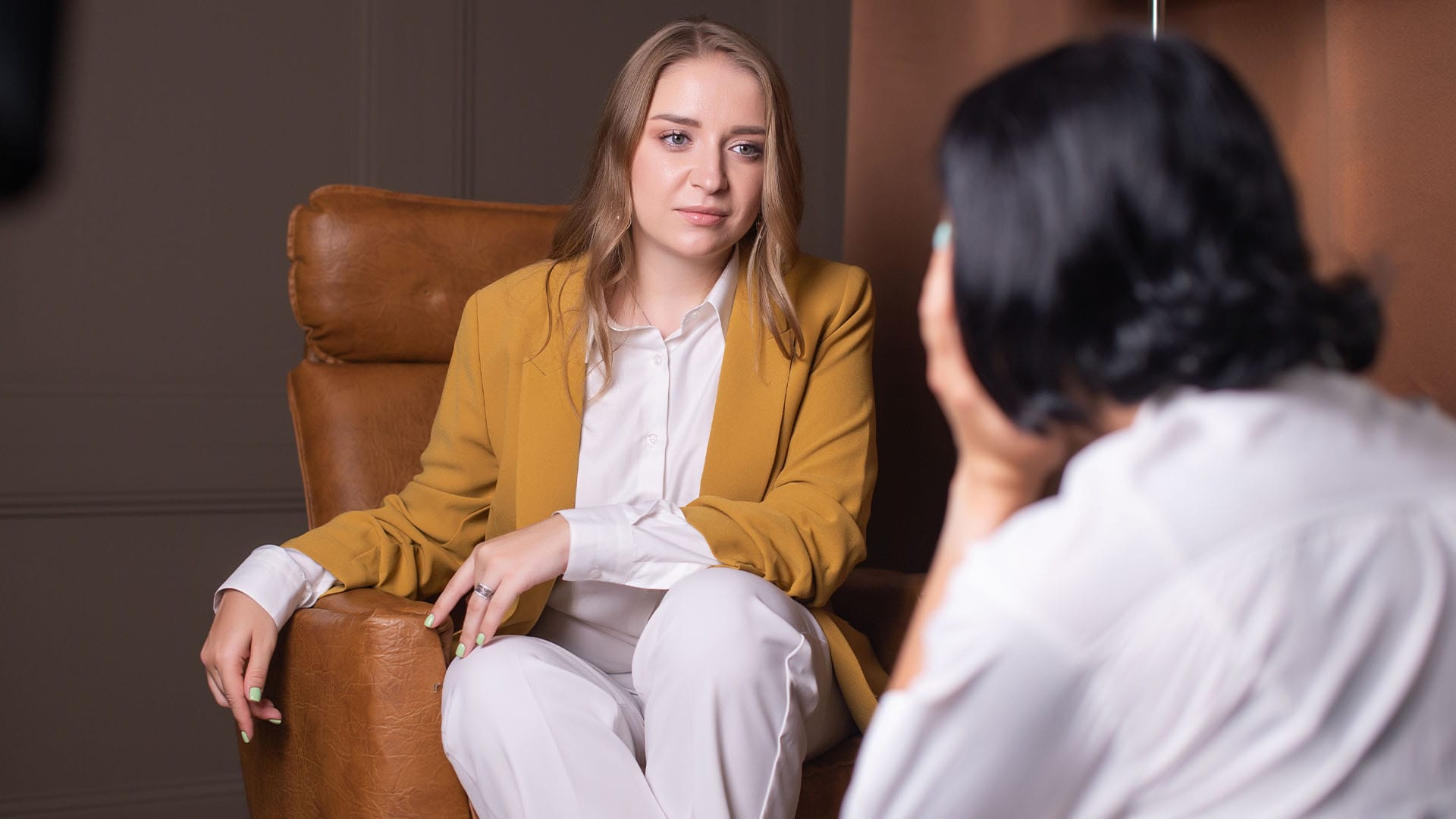 Female therapist in mustard blazer providing burnout therapy to a tech executive in Silicon Valley.