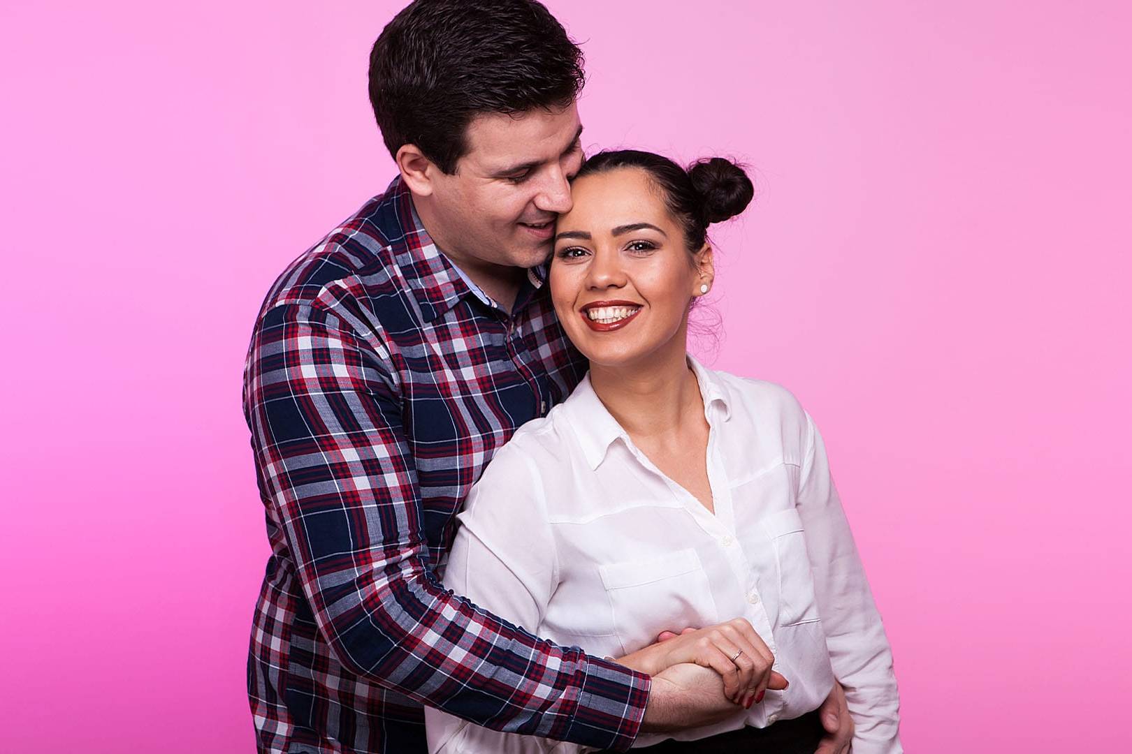 Smiling couple embracing against a pink background, reflecting warmth and happiness after successful couples counseling.
