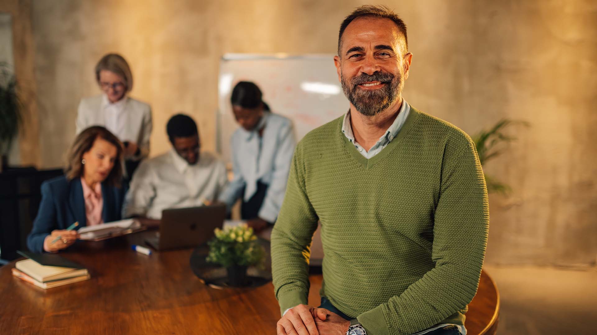 Confident startup founder in modern office with diverse team working in background representing leadership mental health support