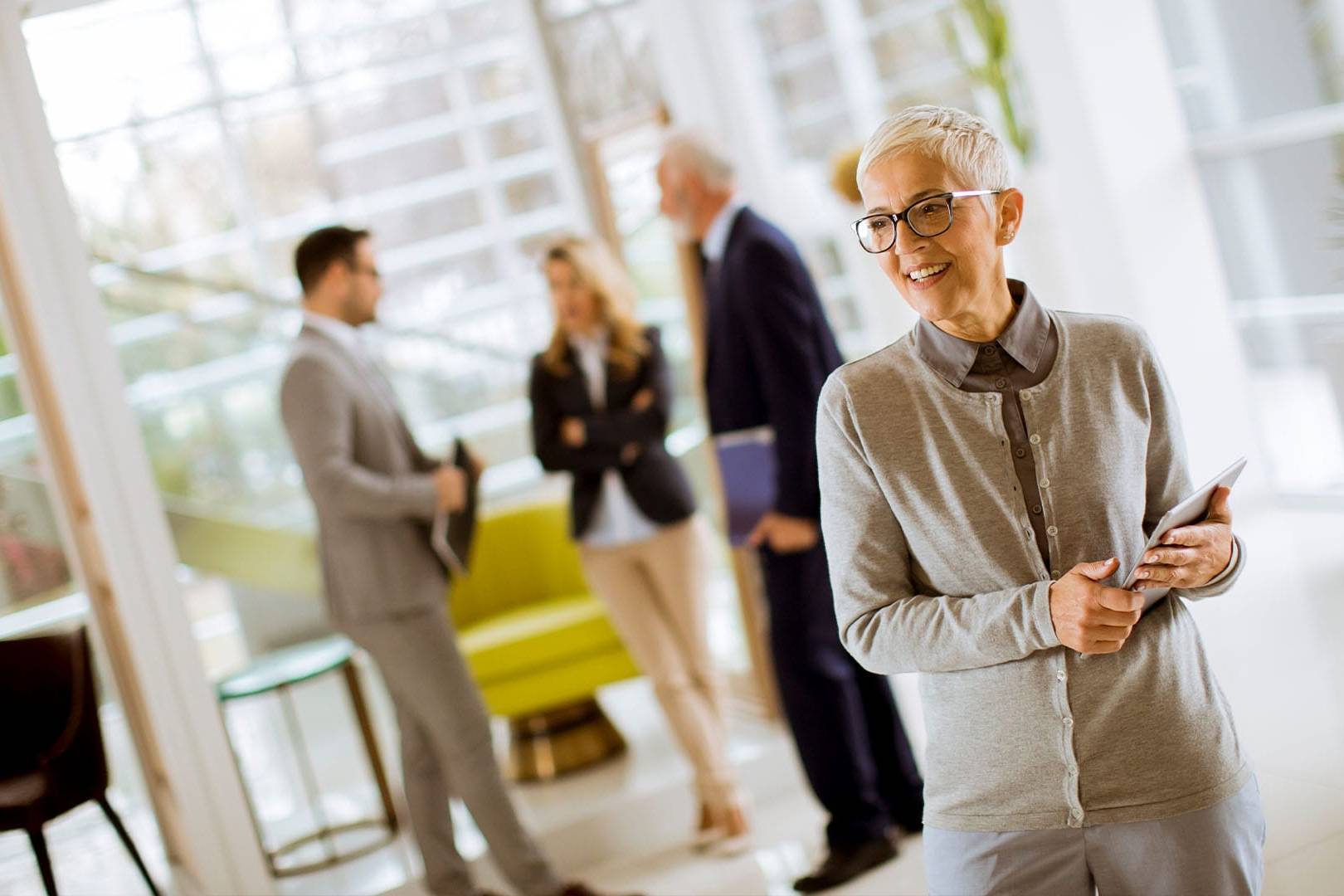 Smiling older professional holding tablet in modern office setting