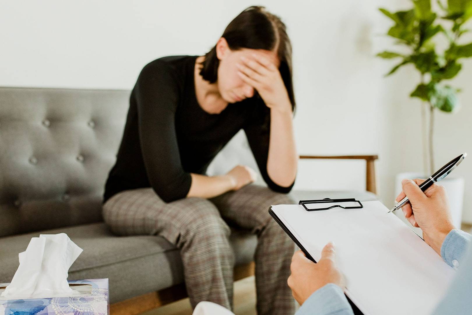Upset woman holding her head while therapist takes notes