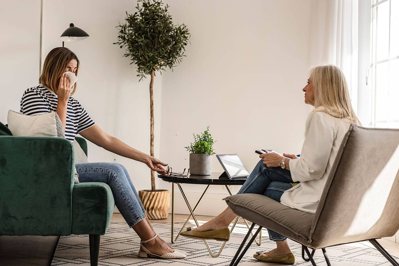 woman in therapy session wiping tears while therapist listens attentively