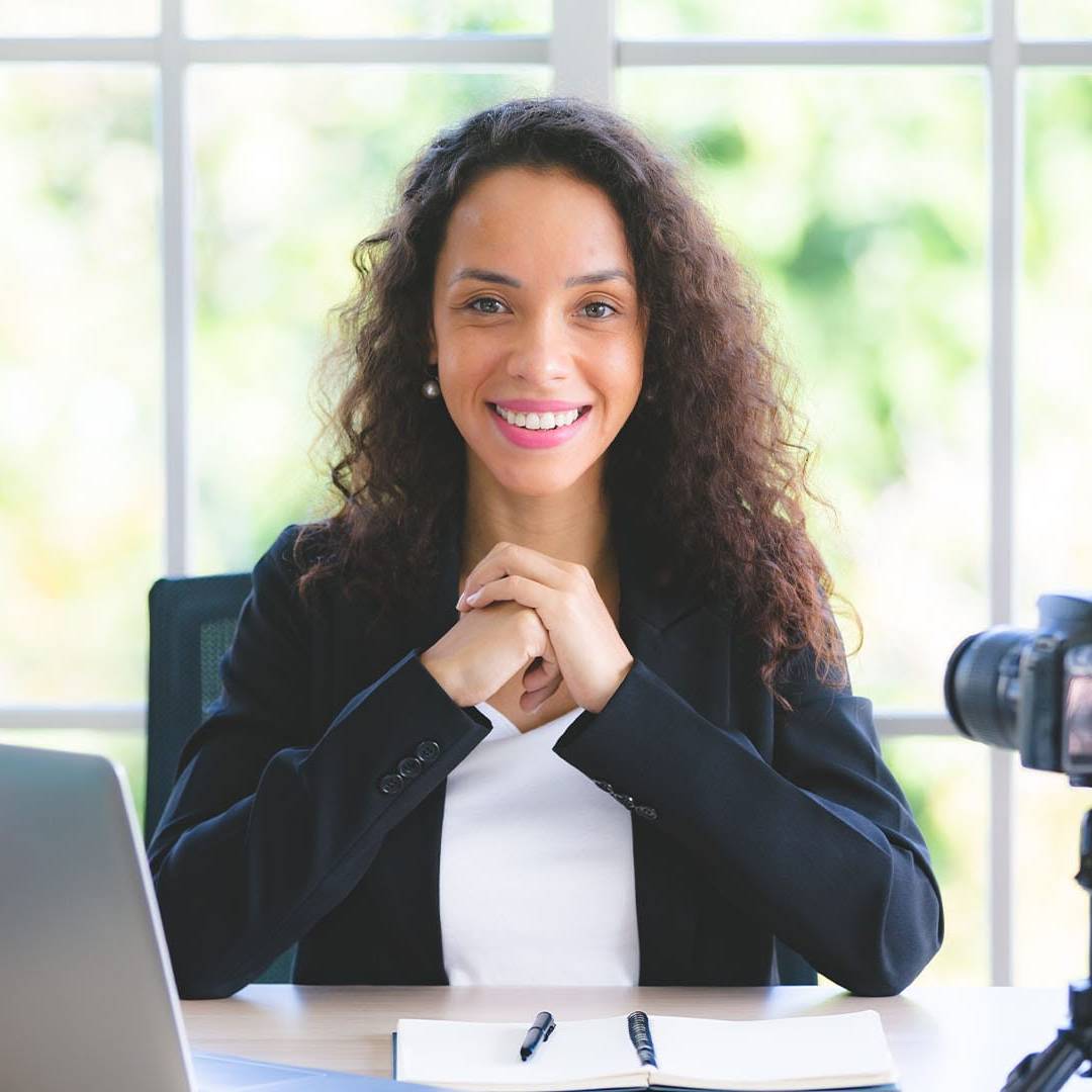 Smiling professional woman at desk with camera and laptop, ready for virtual therapy session