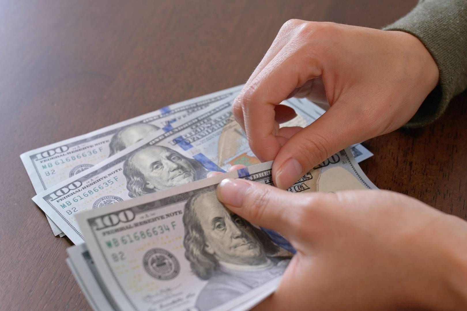 Hands counting hundred-dollar bills, representing the cost comparison between private therapy paid in cash and insurance-based mental health care.