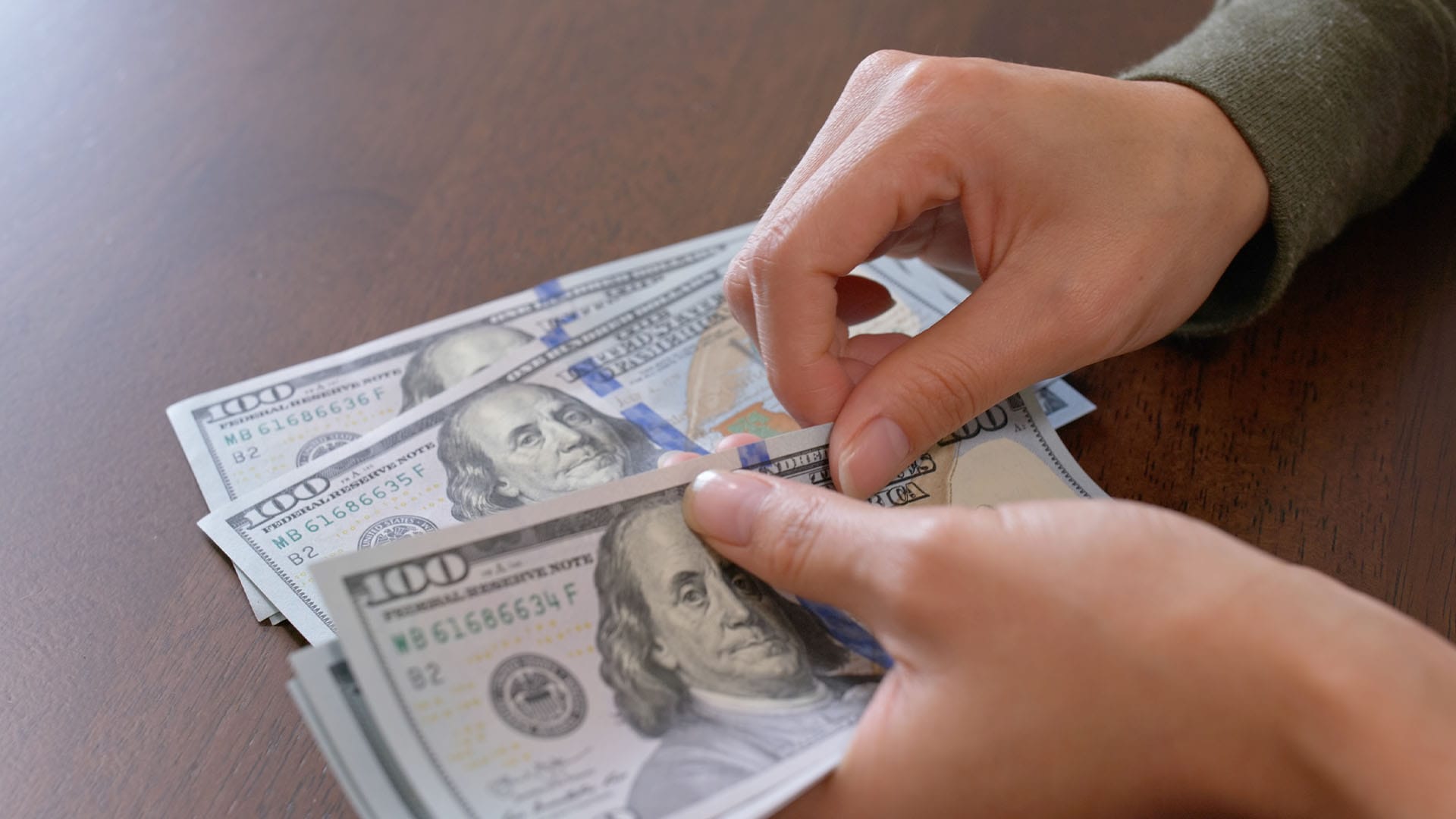 Hands counting hundred-dollar bills, representing the cost comparison between private therapy paid in cash and insurance-based mental health care.