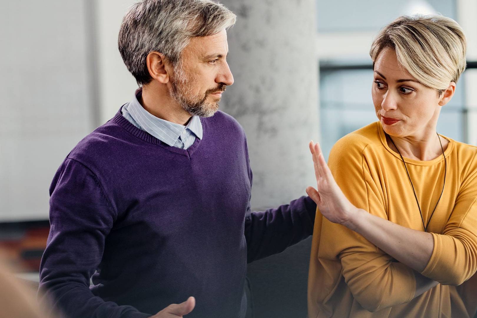 A couple in a tense moment during a counseling session, with the woman holding up her hand as the man attempts to talk.
