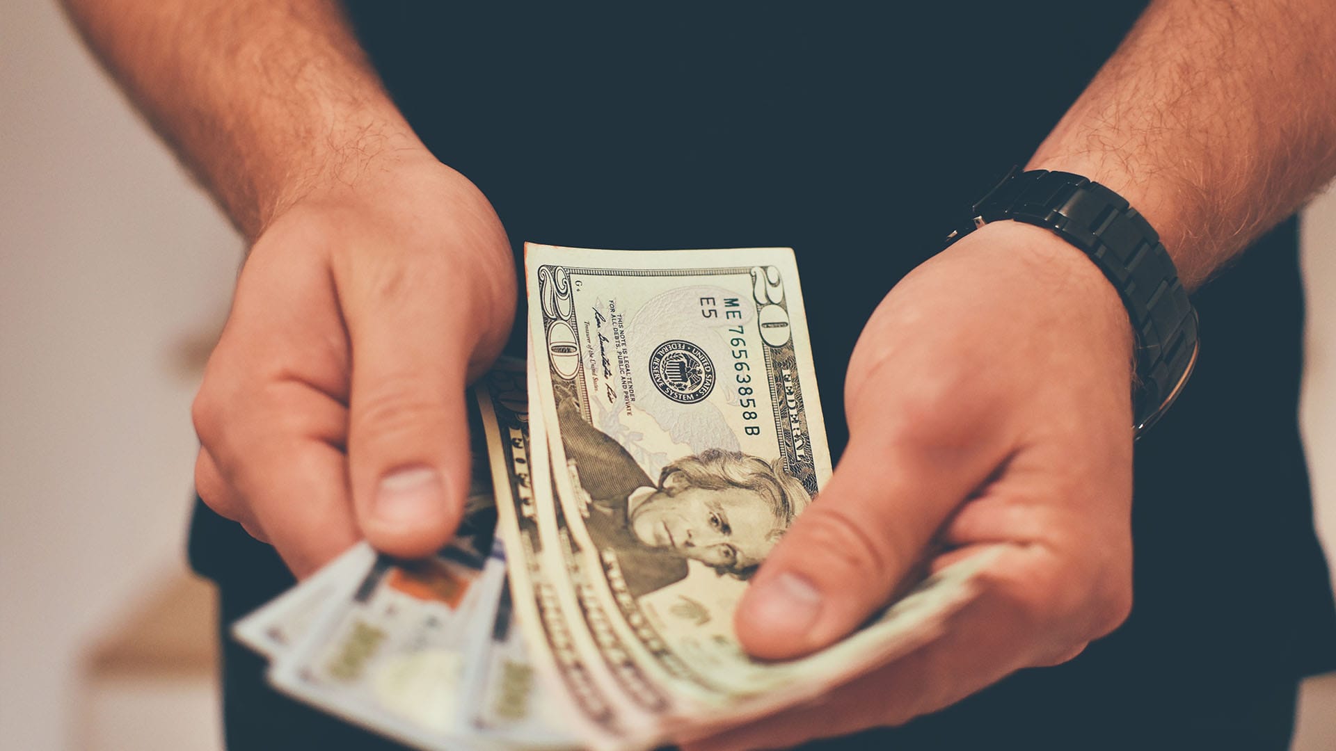 Close-up of a person holding U.S. dollar bills, symbolizing the cost of private counseling for stress and burnout in California.
