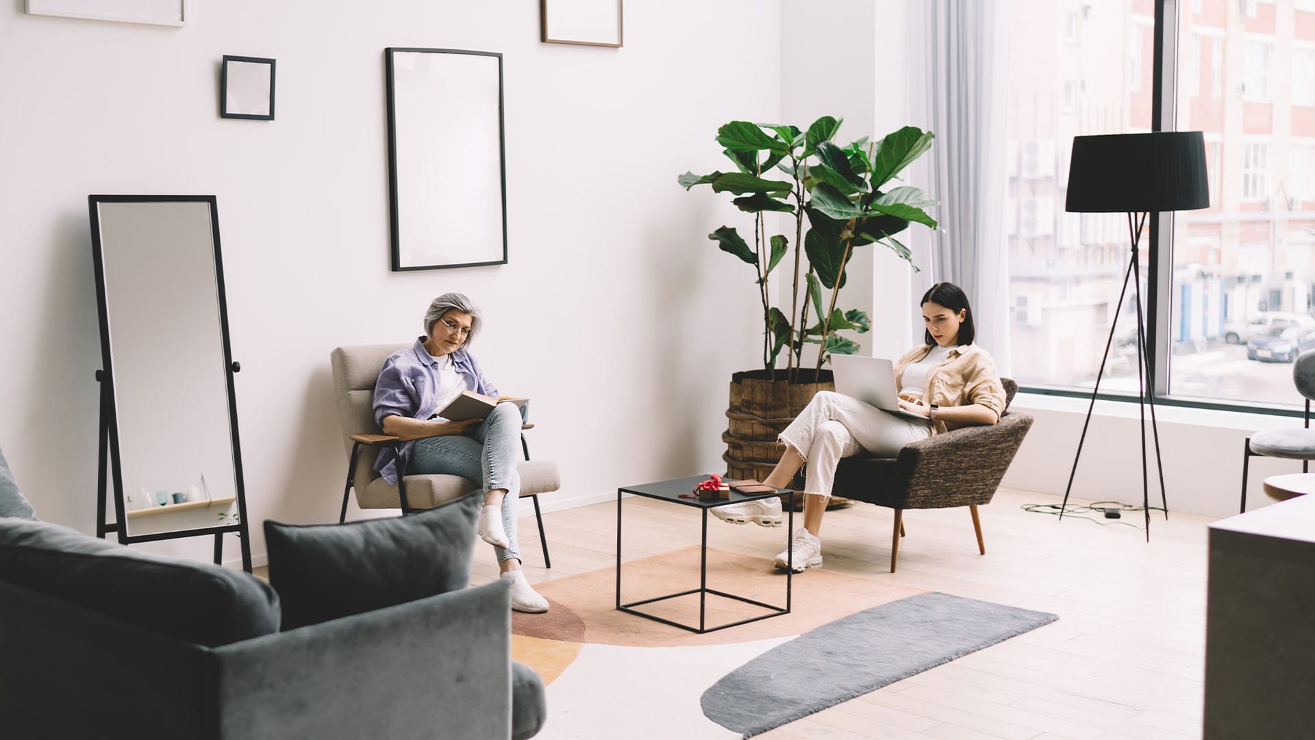 two women sitting in modern therapy office, one reading and one using laptop