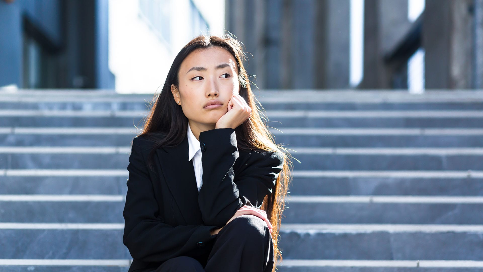 Professional woman sitting on steps looking thoughtful, symbolizing the need for discreet online therapy sessions in Newport Beach.