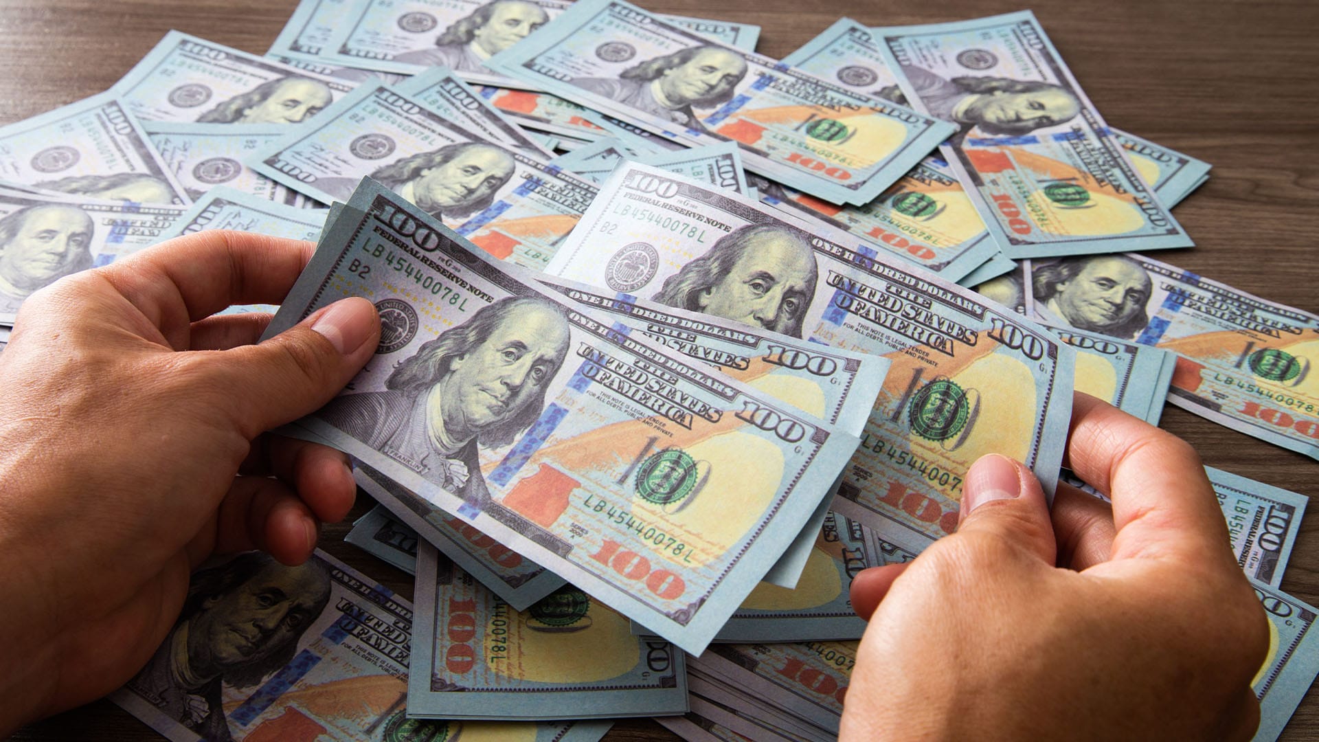 Hands holding stacks of hundred-dollar bills, symbolizing the flexibility and faster access that private pay therapy offers in California.