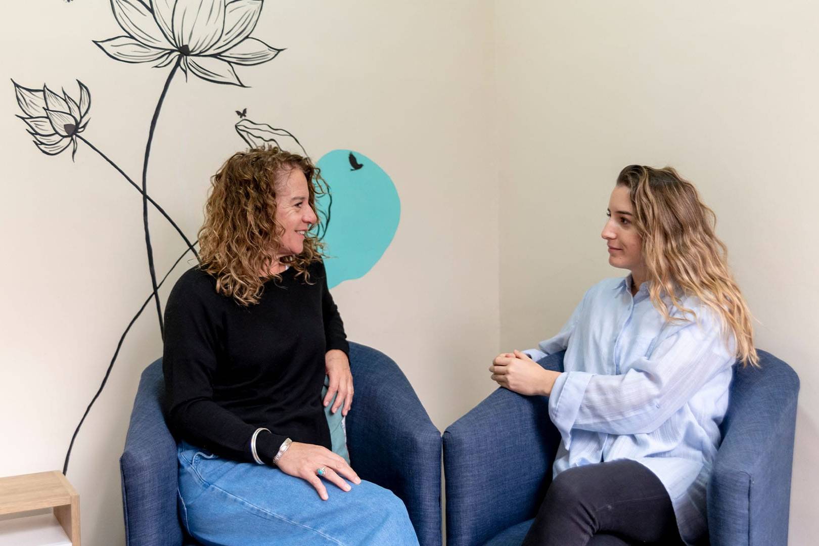 two women sitting in blue chairs having a private conversation in therapy setting