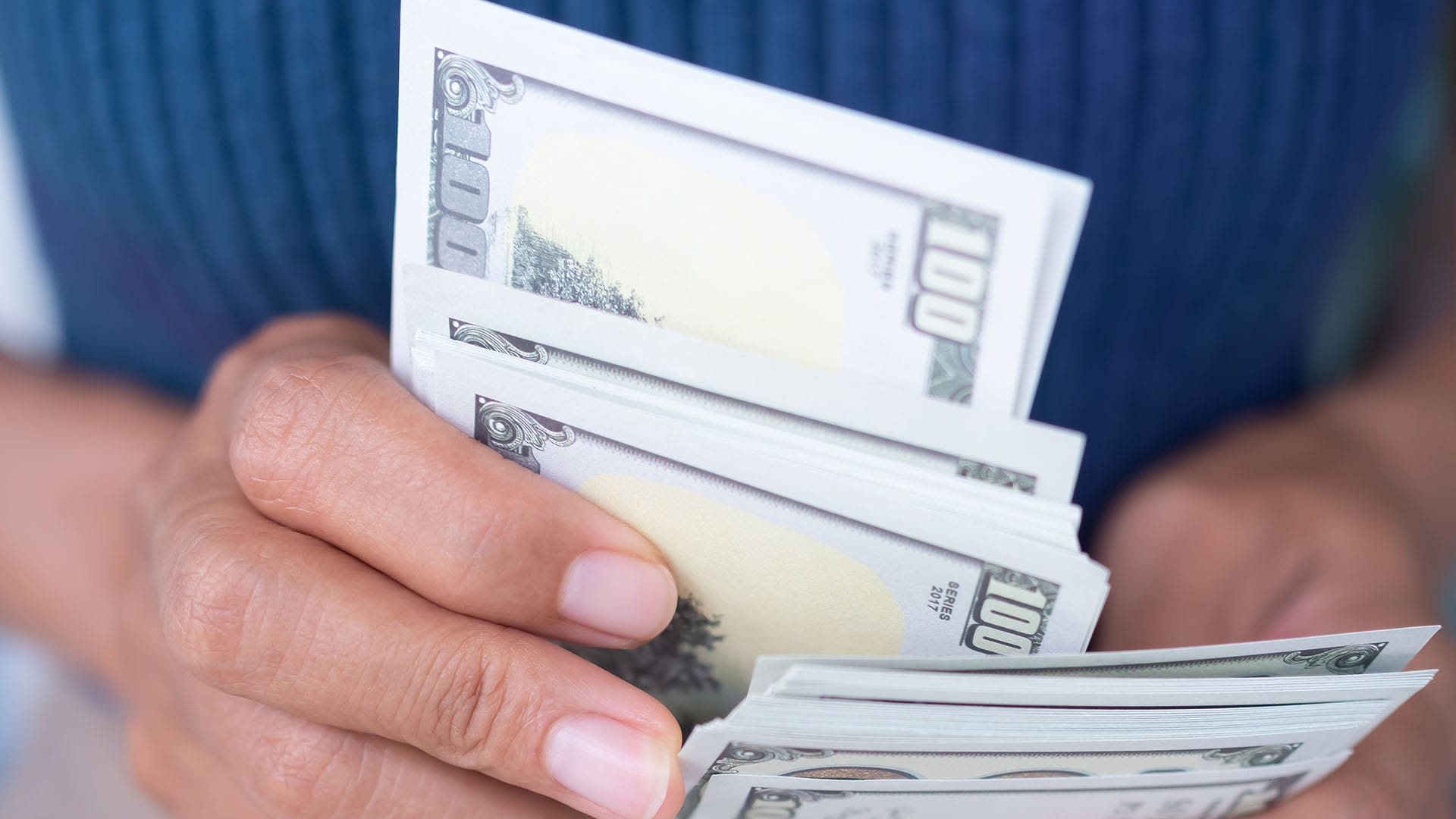 Close-up of hands holding a stack of hundred-dollar bills, symbolizing the financial decision behind choosing out-of-network therapy in California.