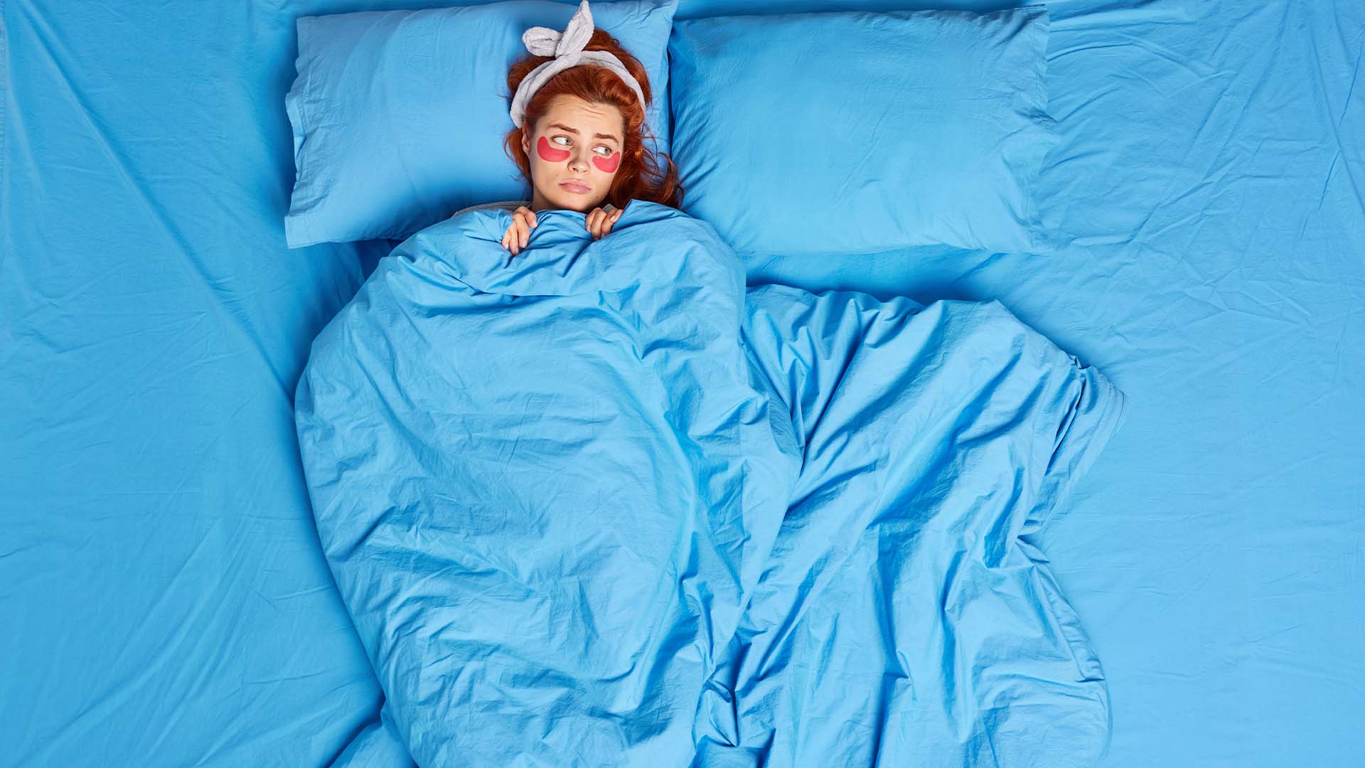 Exhausted professional woman awake in bed with eye masks representing work-related insomnia and sleep disturbance