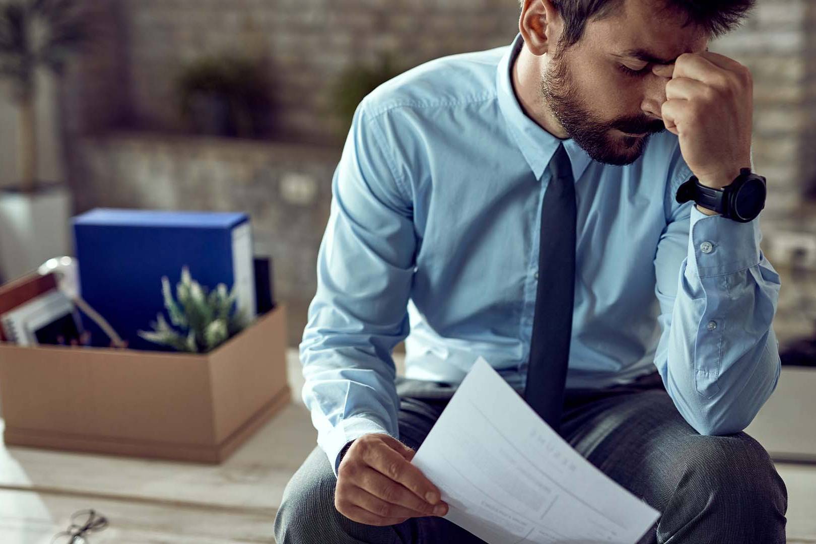 Distressed professional sitting with head down and packed belongings box nearby, representing anxiety and career stress experienced by high-achieving individuals