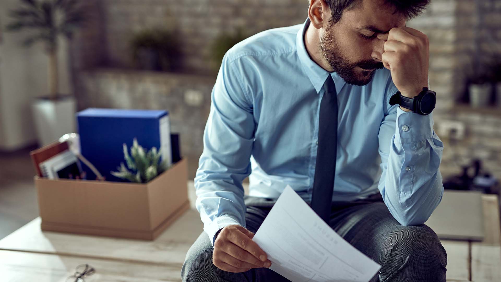 Distressed professional sitting with head down and packed belongings box nearby, representing anxiety and career stress experienced by high-achieving individuals