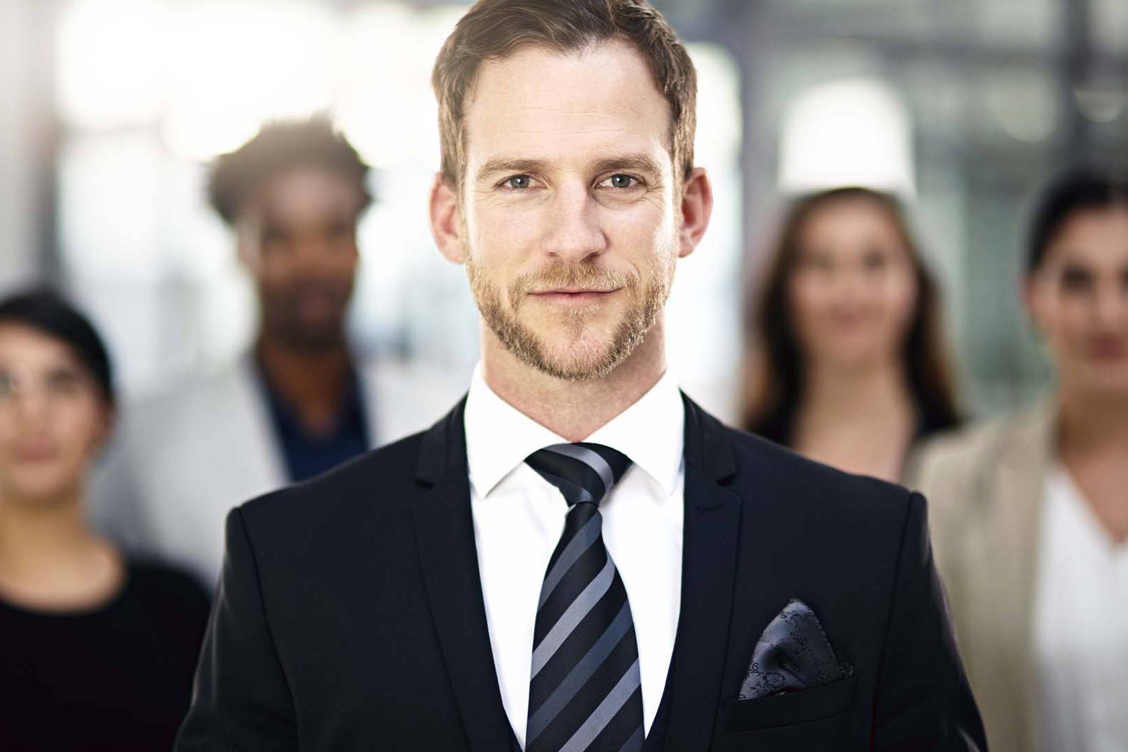 Professional businessman in suit standing confidently with diverse team in modern Orange County office