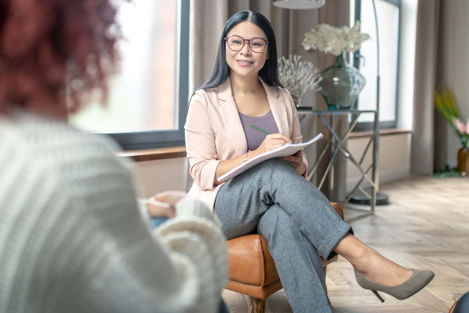 Smiling therapist with glasses taking notes during session with client in cozy office
