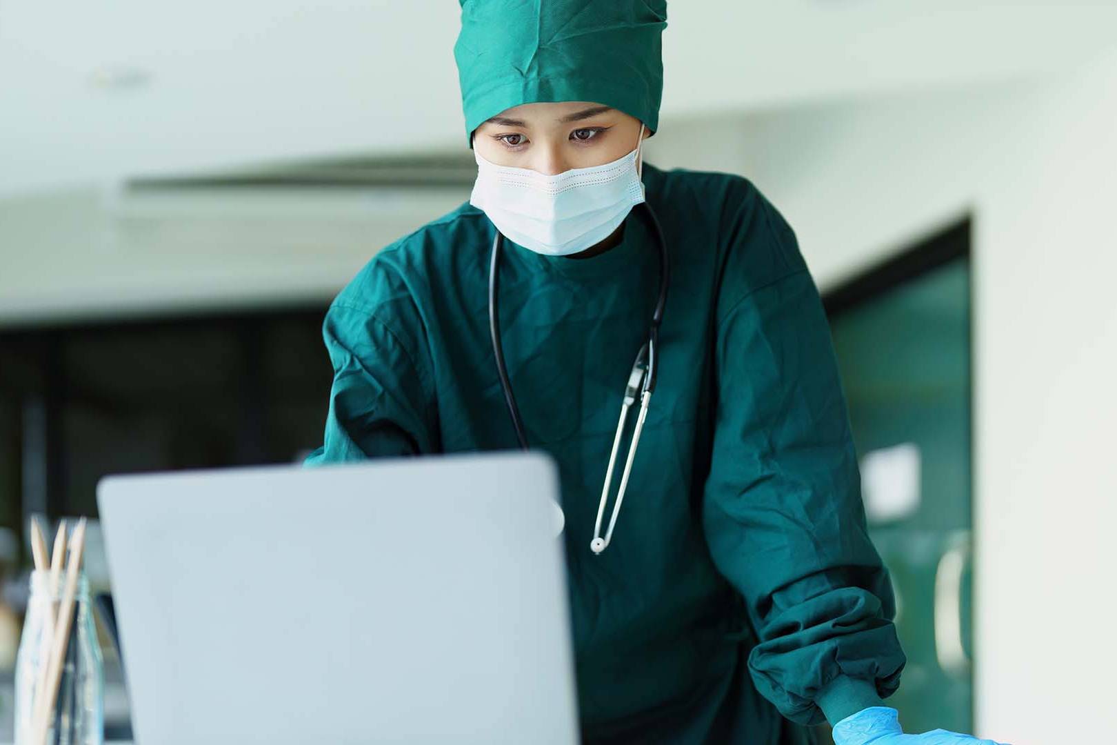 Surgeon in full surgical attire with mask and cap working at computer, representing physicians seeking confidential therapy without medical board reporting concerns